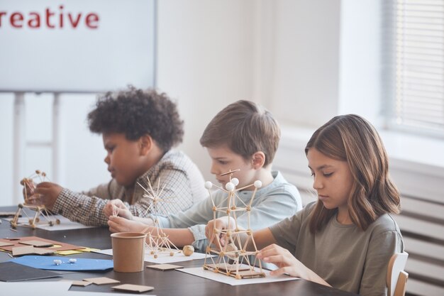 Children building STEM structures with sticks and foam balls at a classroom table during a creative learning activity.
